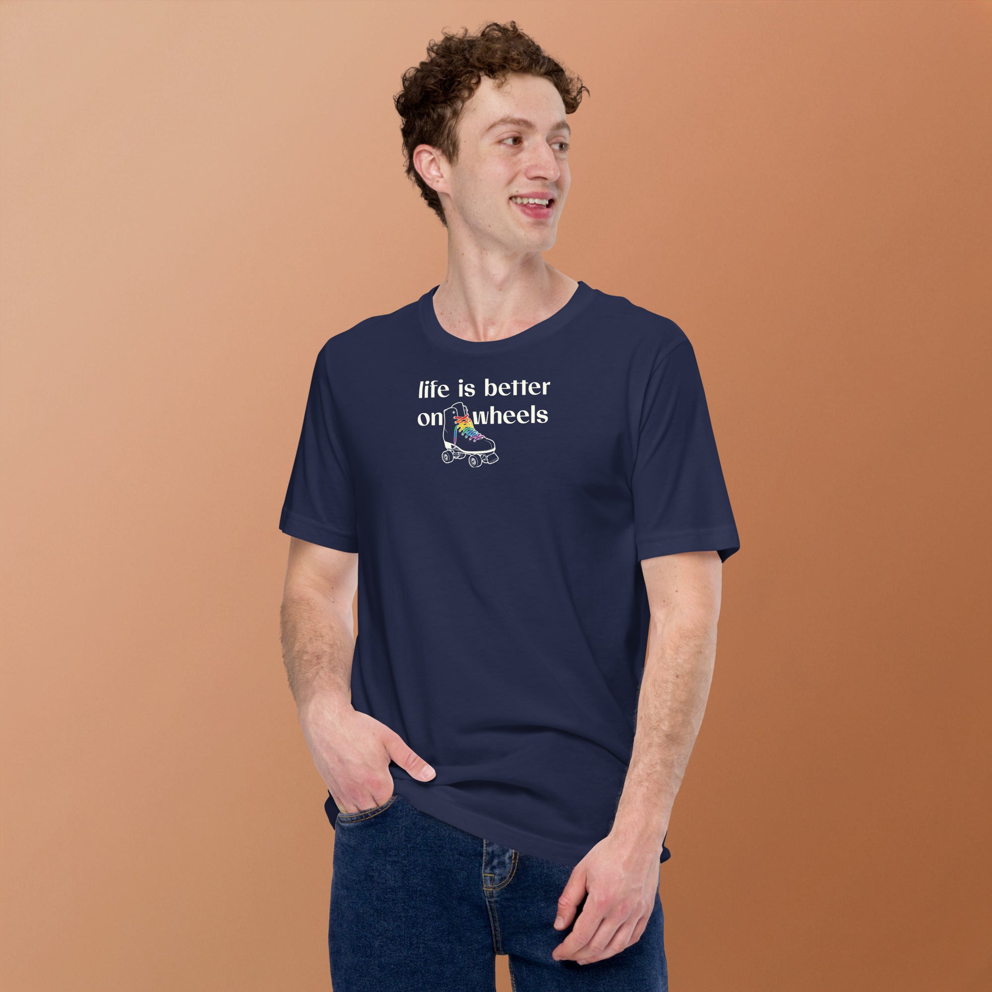 Model wearing Minimalist off white typography life is better on wheels with a small silhouette of a roller skate with LGBTQ+ laces. On navy unisex Bella + Canvas tee. High center chest