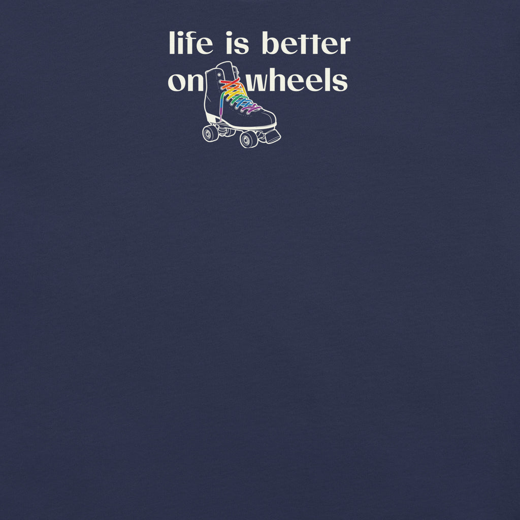 Close up view of minimalist off white typography life is better on wheels with a small silhouette of a roller skate with LGBTQ+ laces. On navy unisex Bella + Canvas tee. High center chest