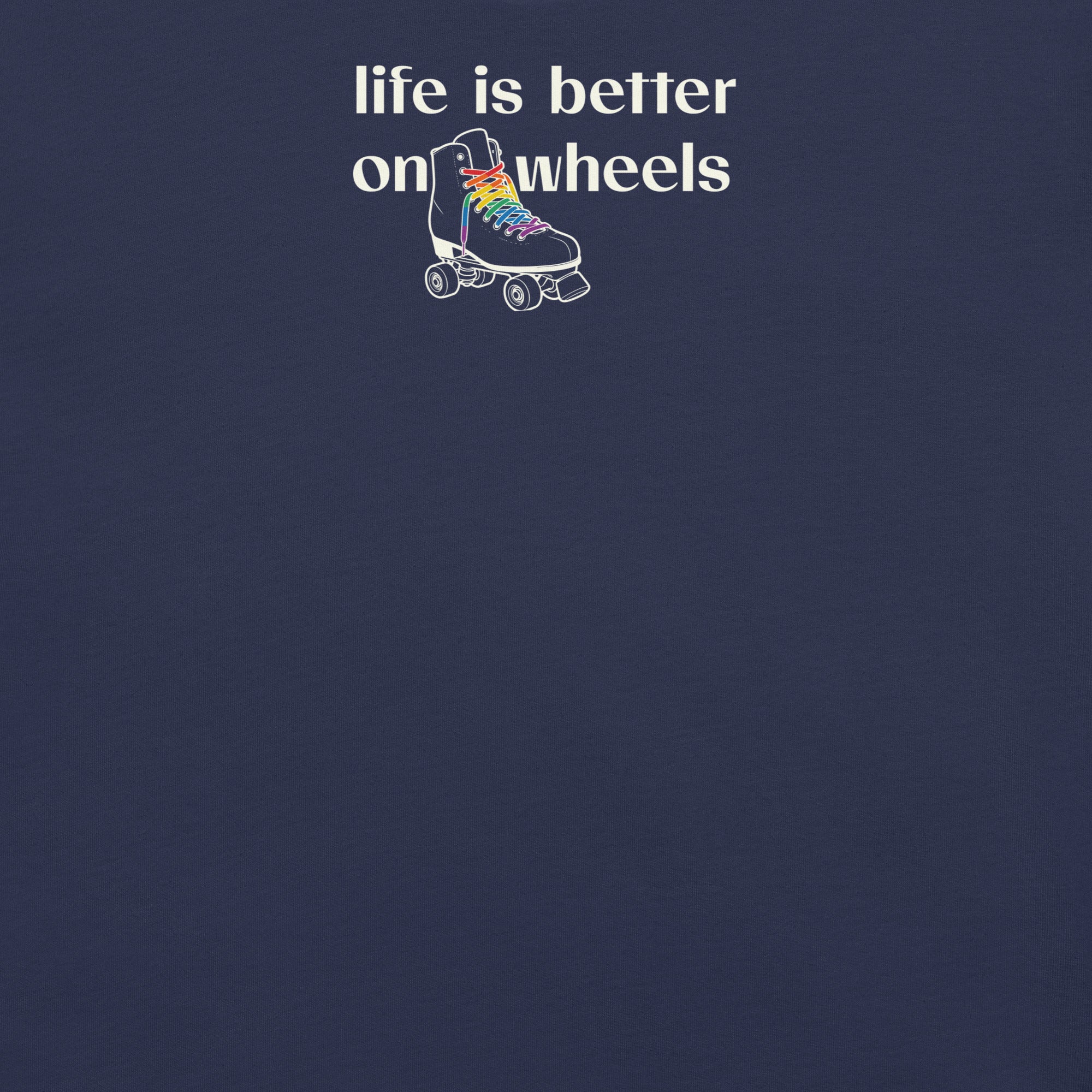 Close up view of minimalist off white typography life is better on wheels with a small silhouette of a roller skate with LGBTQ+ laces. On navy unisex Bella + Canvas tee. High center chest