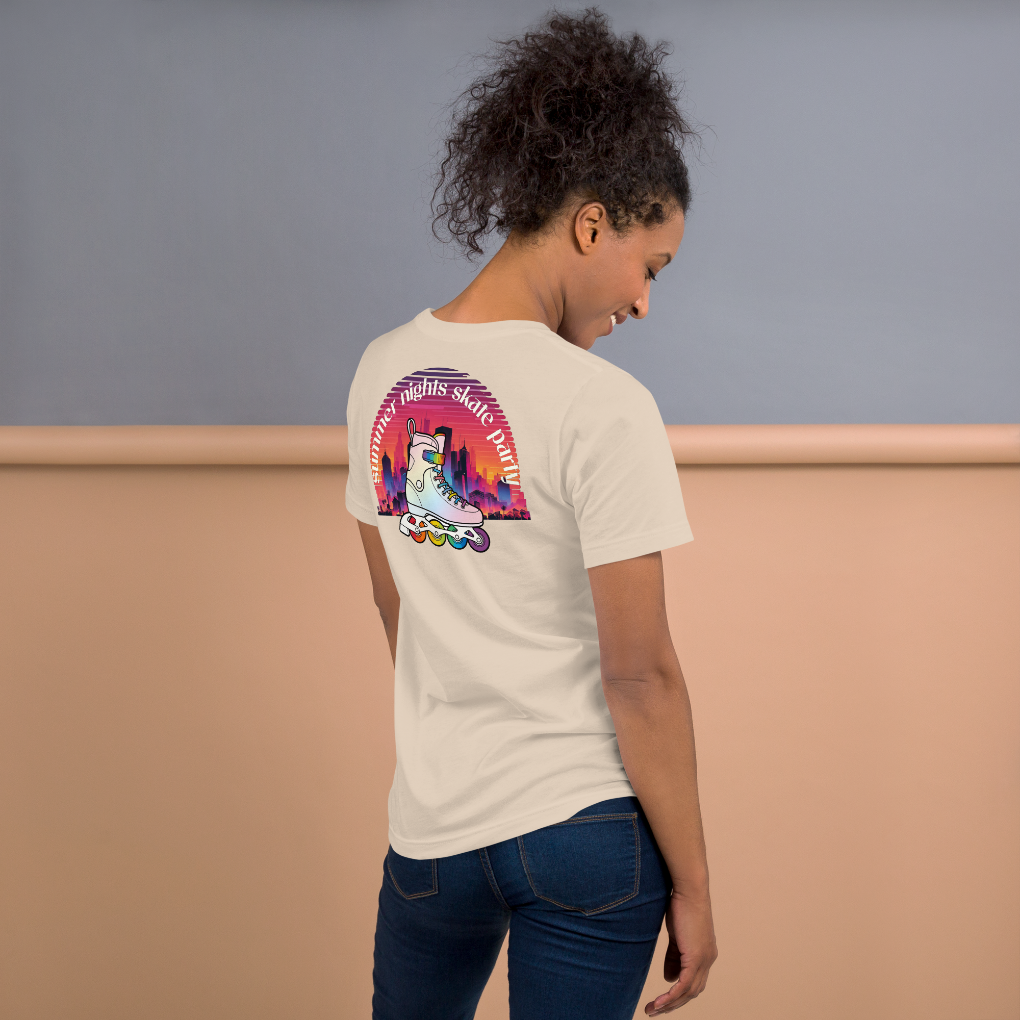 Person wearing beige shirt and jeans. Tshirt features a back print of Summer Nights Skate Party evening sunset and a skyline behind a rainbow roller skate. Printed on unisex Bella + Canvas cotton. 