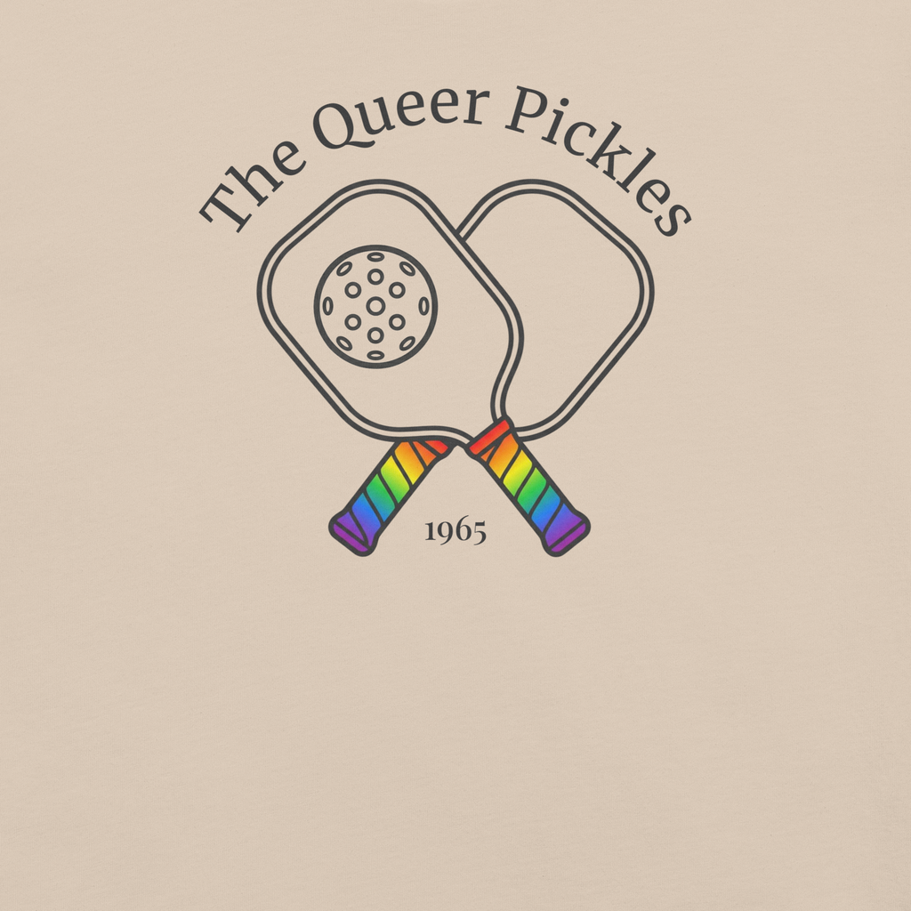The Queer Pickles above 2 crossed paddles with pickleball,  with 1965 club style. Printed on unisex Bella + Canvas cotton beige tshirt. Center Chest black in and rainbow handles. Zoomed in. 