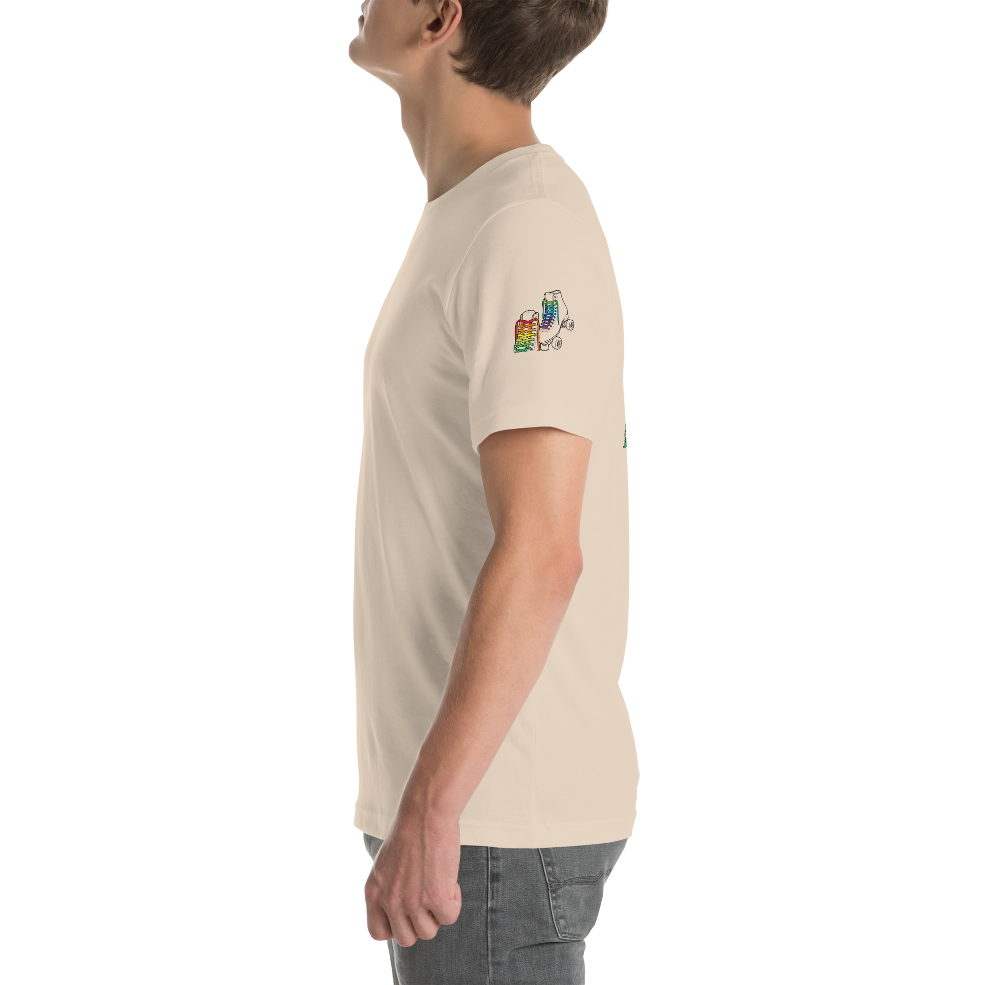 Side view of model wearing beige shirt with outline of 2 quad skates with LGBTQ+ rainbow laces. Printed on left sleeve paired with jeans. Bella + canvas unisex cotton